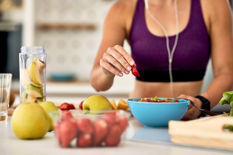 Fotografia da região do peitoral de uma mulher de cropped fitness, comendo uma salada.