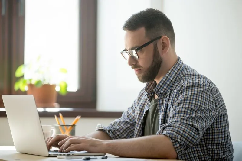 Imagem de um homem branco, de óculos, trabalhando com um notebook