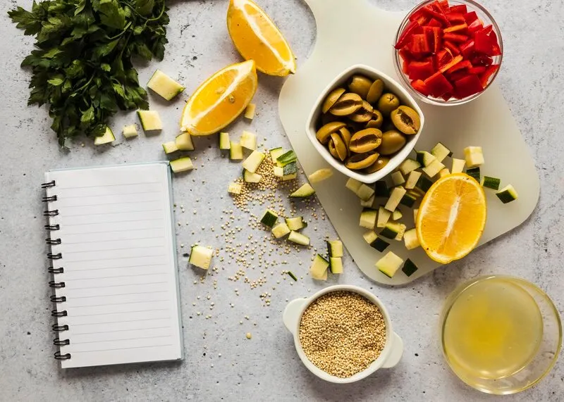 Fotografia de uma mesa com um caderno, ervas, frutas e um chá.