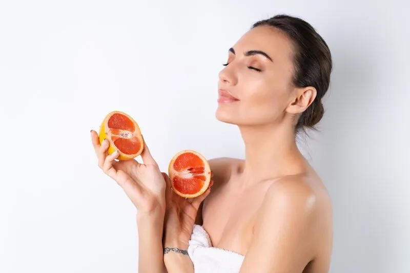 Mulher branca, de coque, segurando duas metades de laranja, de olhos fechados