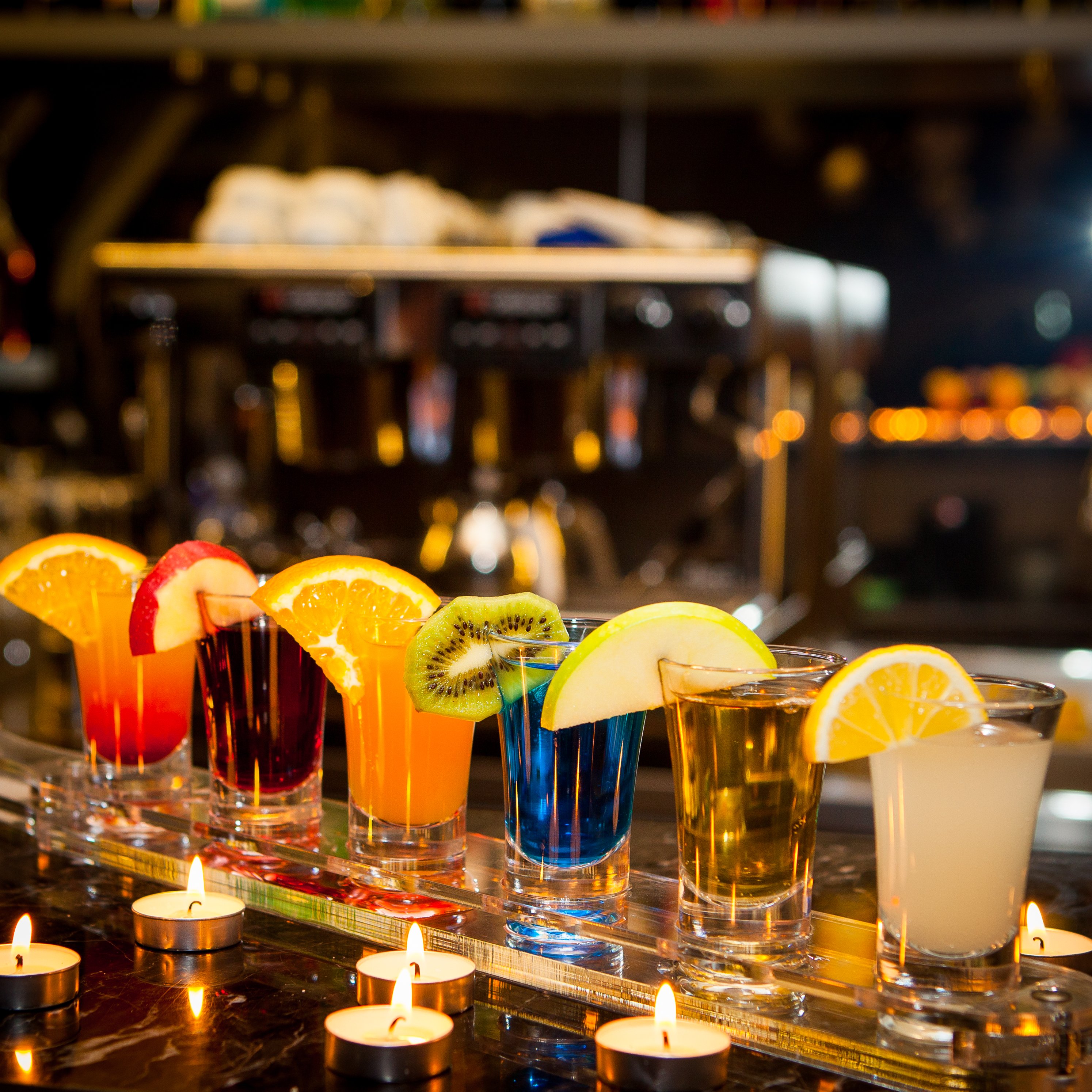 side-view-cocktail-shots-with-slice-lemon-kiwi-slice-candles-bar